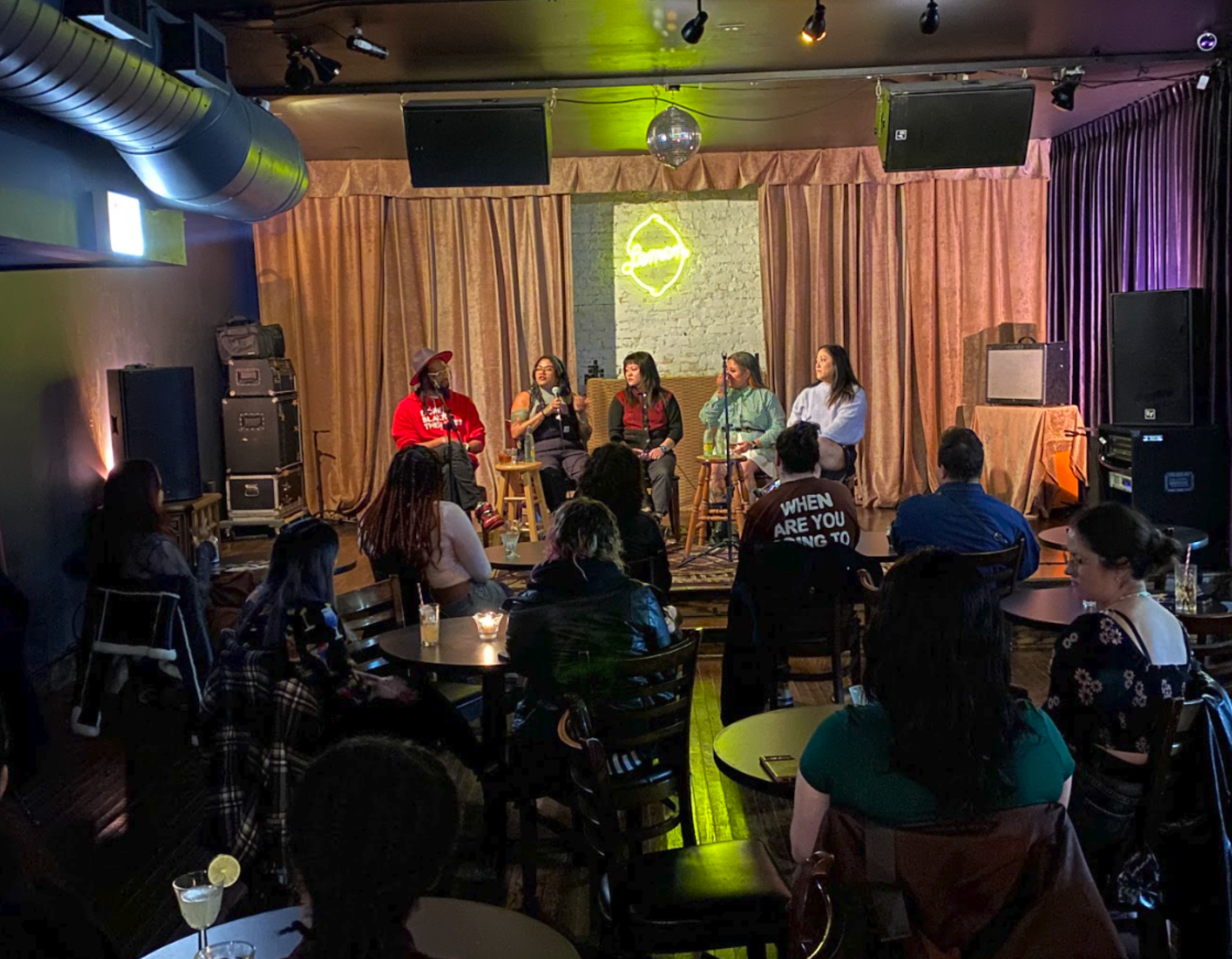 a dimly lit bar environment with a panel of five people on stage