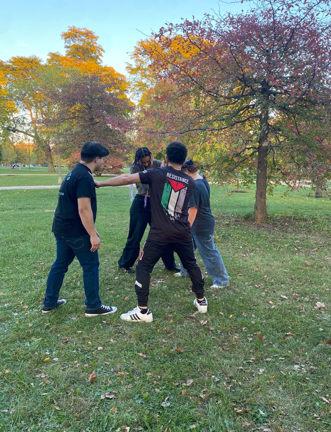 four people demonstrate self defense moves on green grass out in the open with a tree in the background