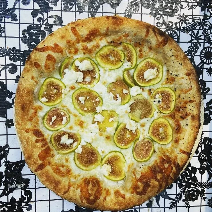 Yellow squash pizza with cheese on a black and white floral patterned surface.