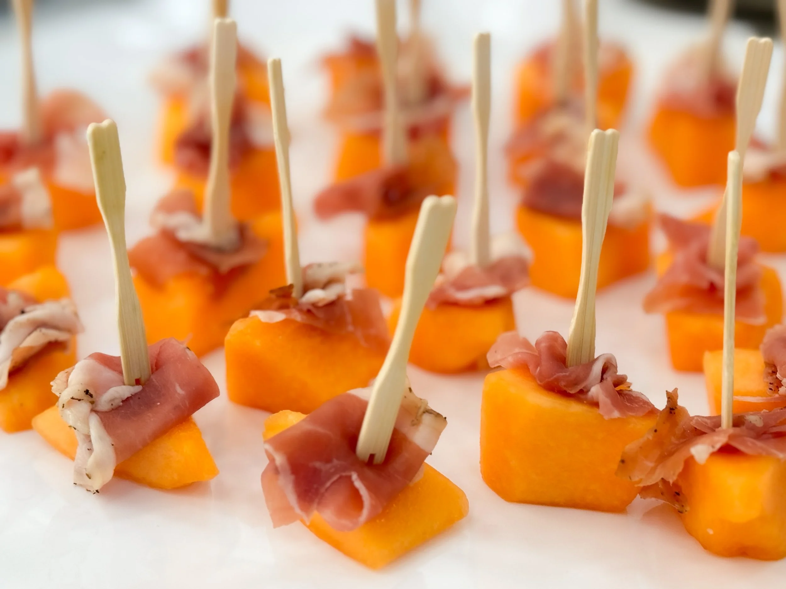 Canapés consisting of cantaloupe slices wrapped with prosciutto and secured with toothpicks.