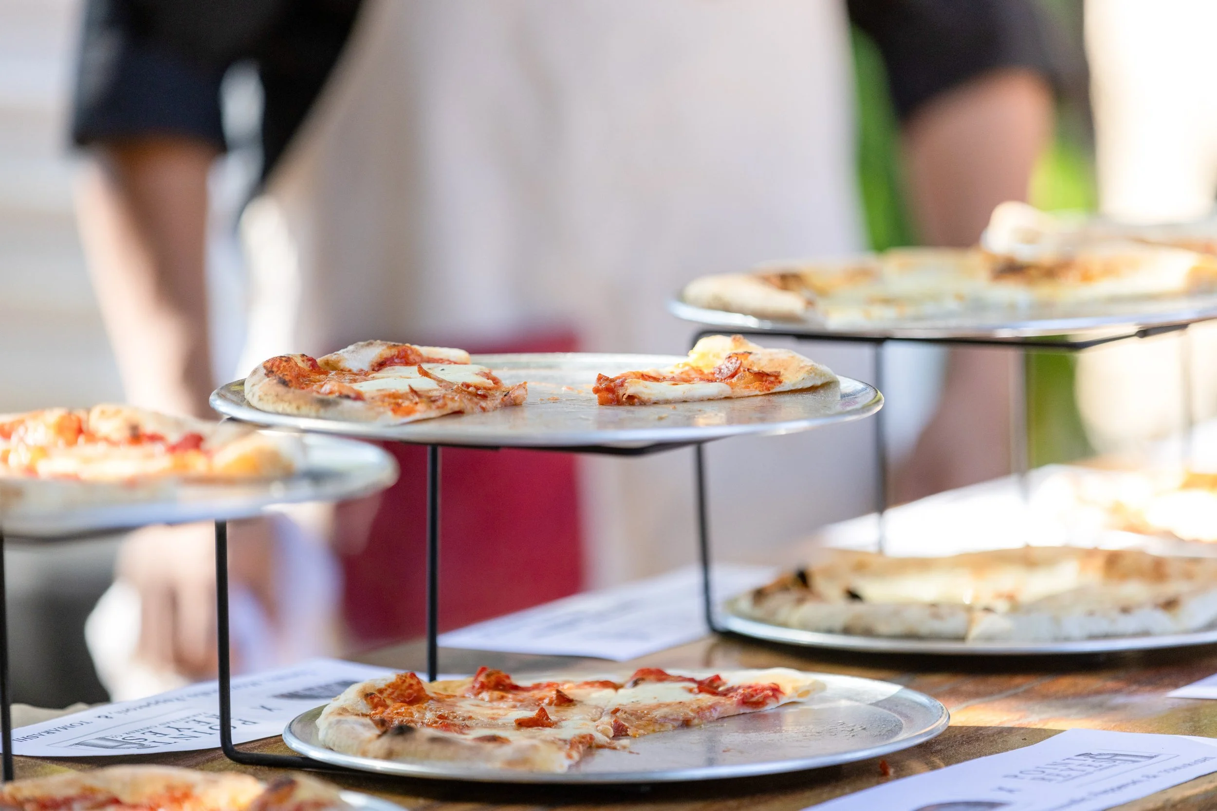 Multiple slices of pizza on metal stands at a pizza tasting event.