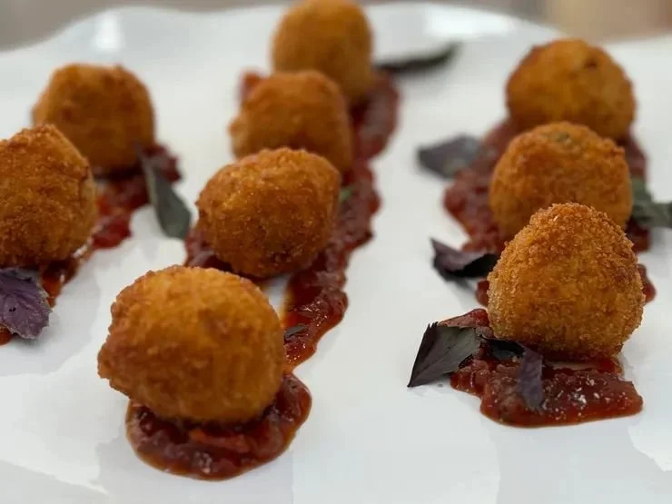 Crispy fried croquettes on a bed of red sauce with purple basil leaves, arranged on white plate.