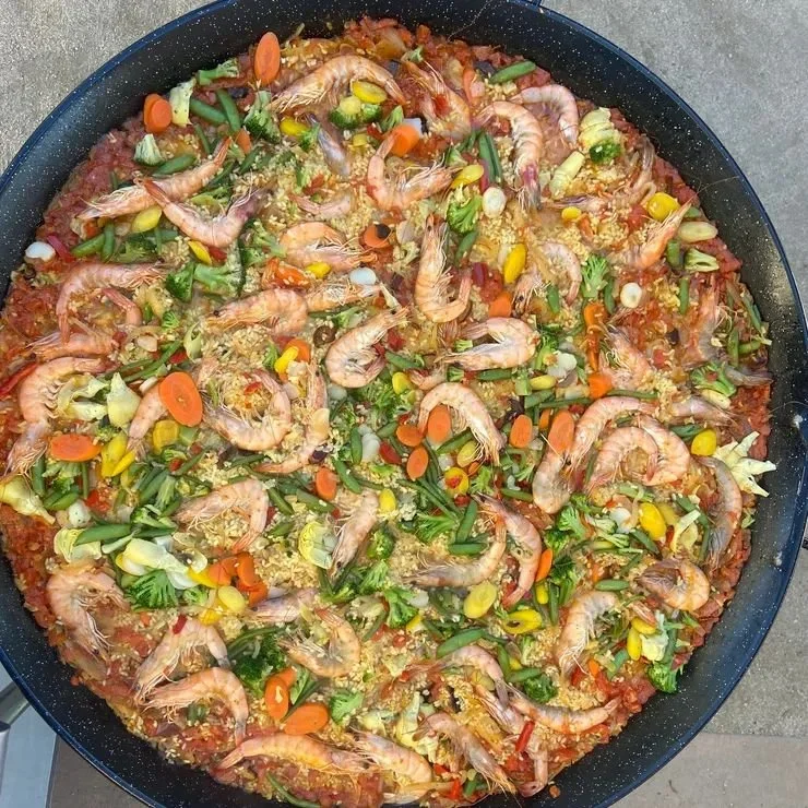 Preparation of shrimp and vegetable stir-fry in a large black pan, with visible shrimp, carrots, green onions, and other vegetables.