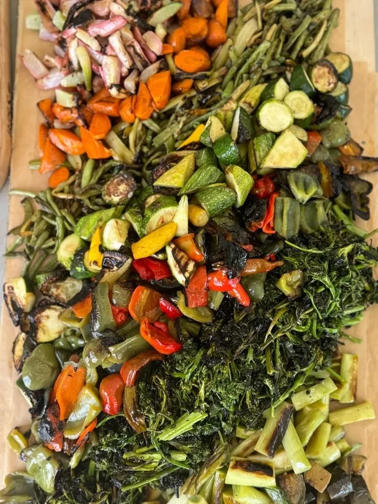 Assorted grilled vegetables on a wooden board, including carrots, zucchini, bell peppers, and greens.