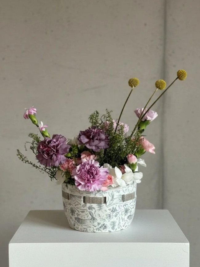 A floral arrangement in a decorative white and gray vase placed on a white surface against a gray wall by Dallas wedding florist Izalena Floral House.