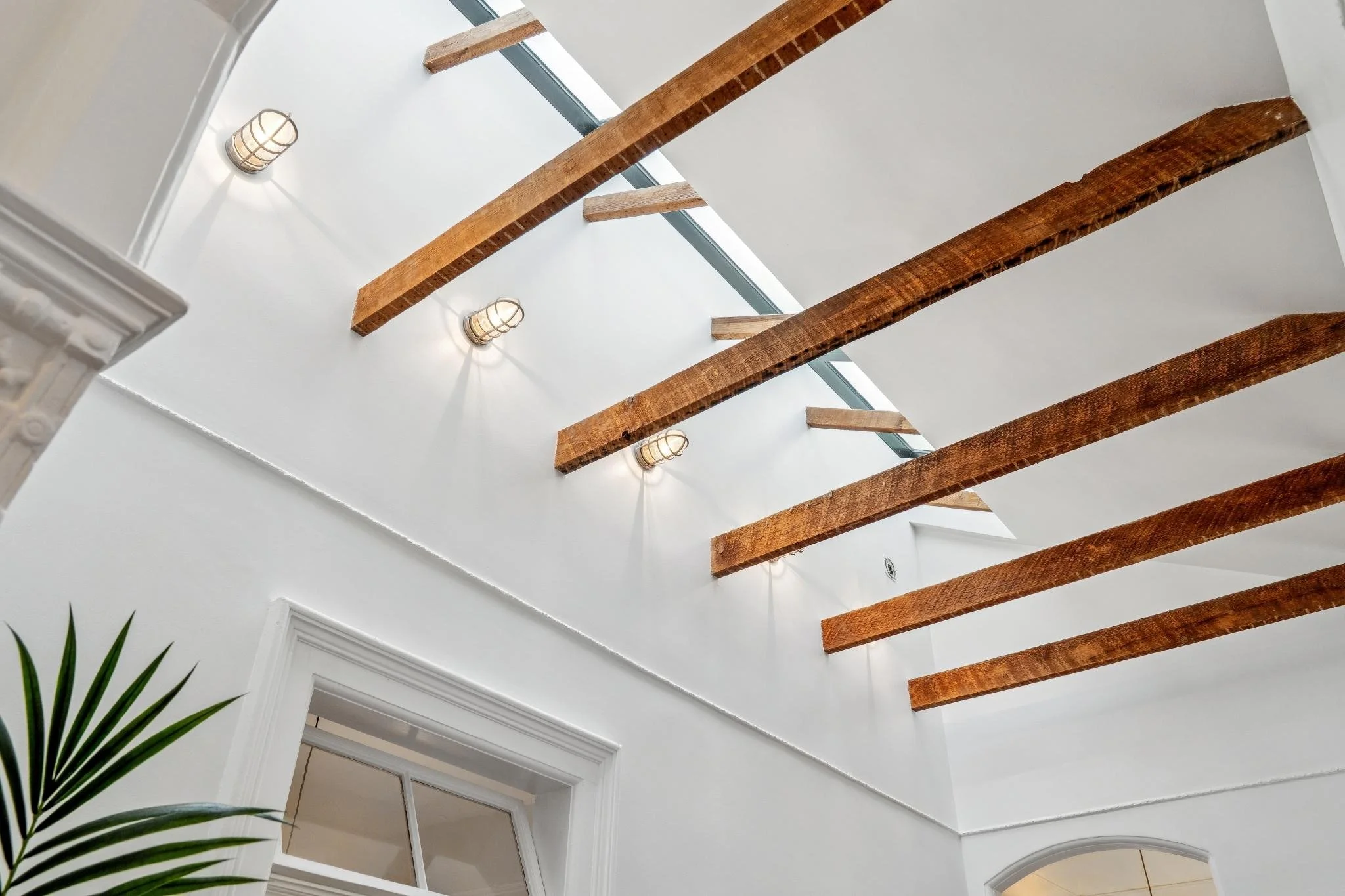 Interior ceiling with exposed wooden beams, wall-mounted lights, and a skylight window.