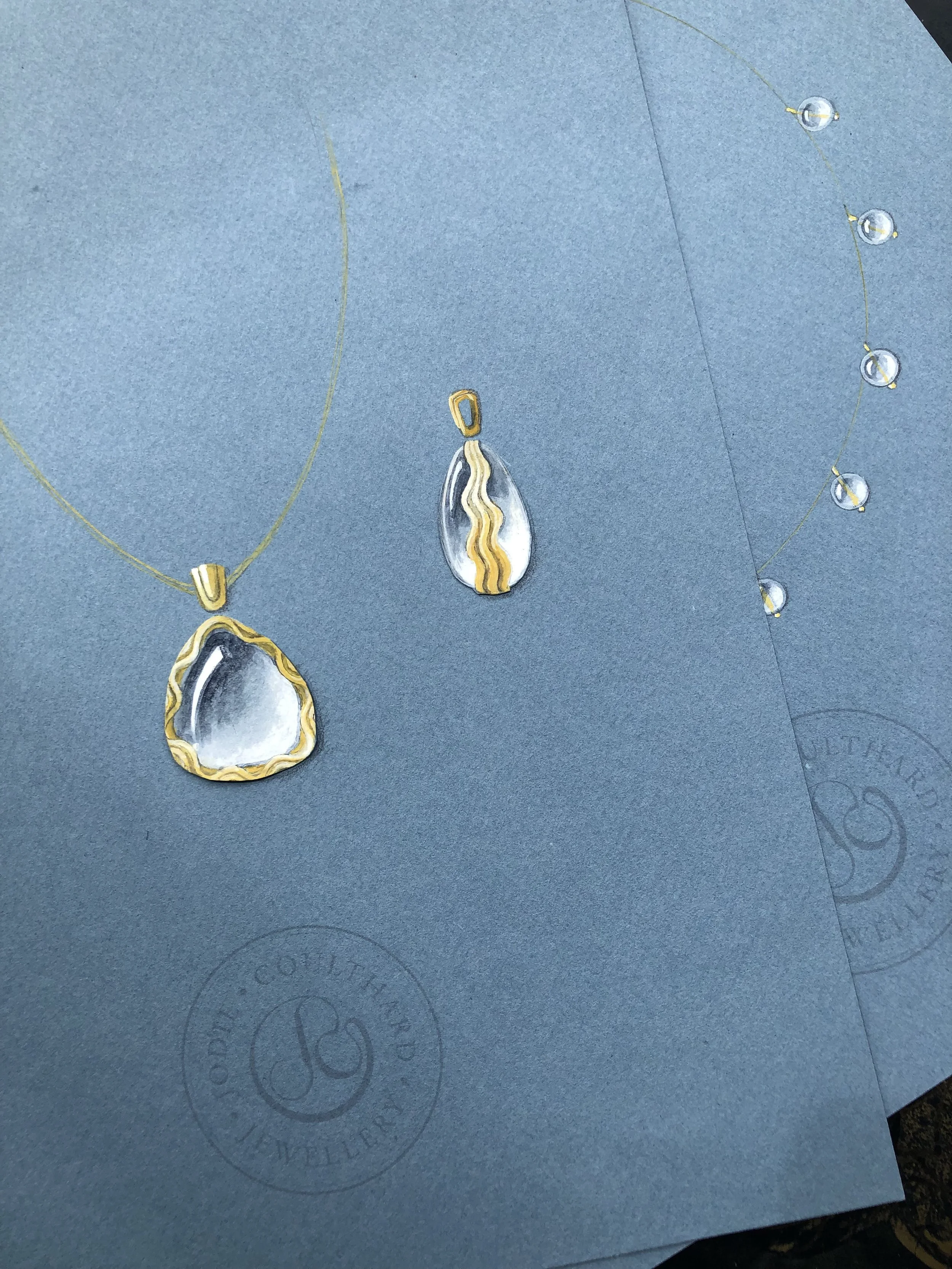 Close-up of a necklace with a pendant shaped like a geode with gold-colored accents, lying on gray paper with circular and partial logo markings.