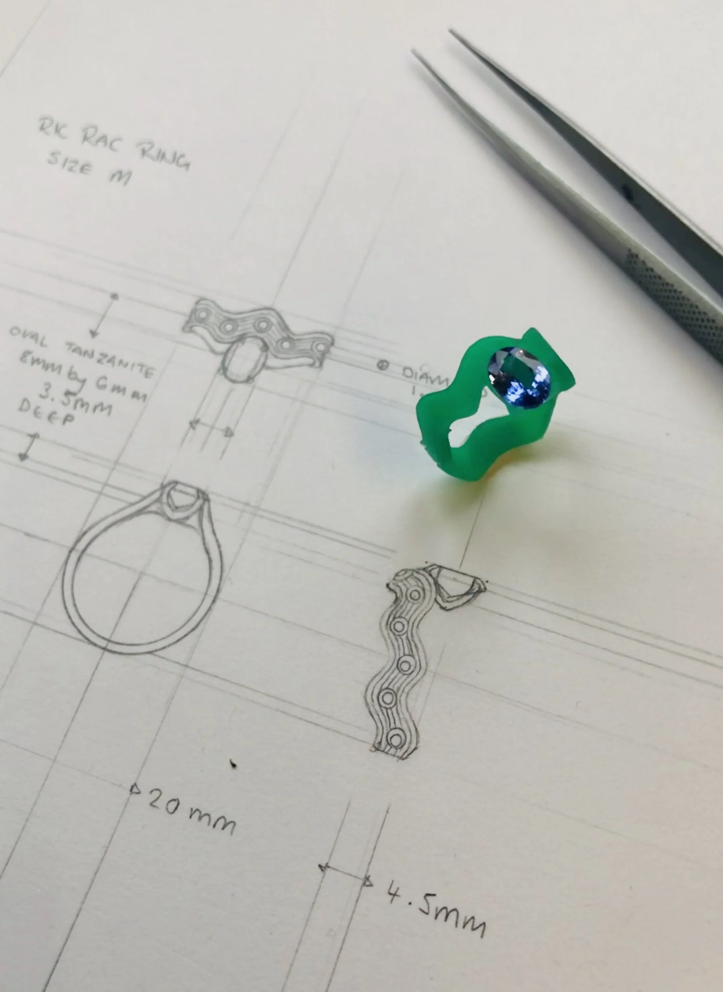 Technical drawing of a bicycle component with annotations, a small green rubber ring, and a blue gemstone.