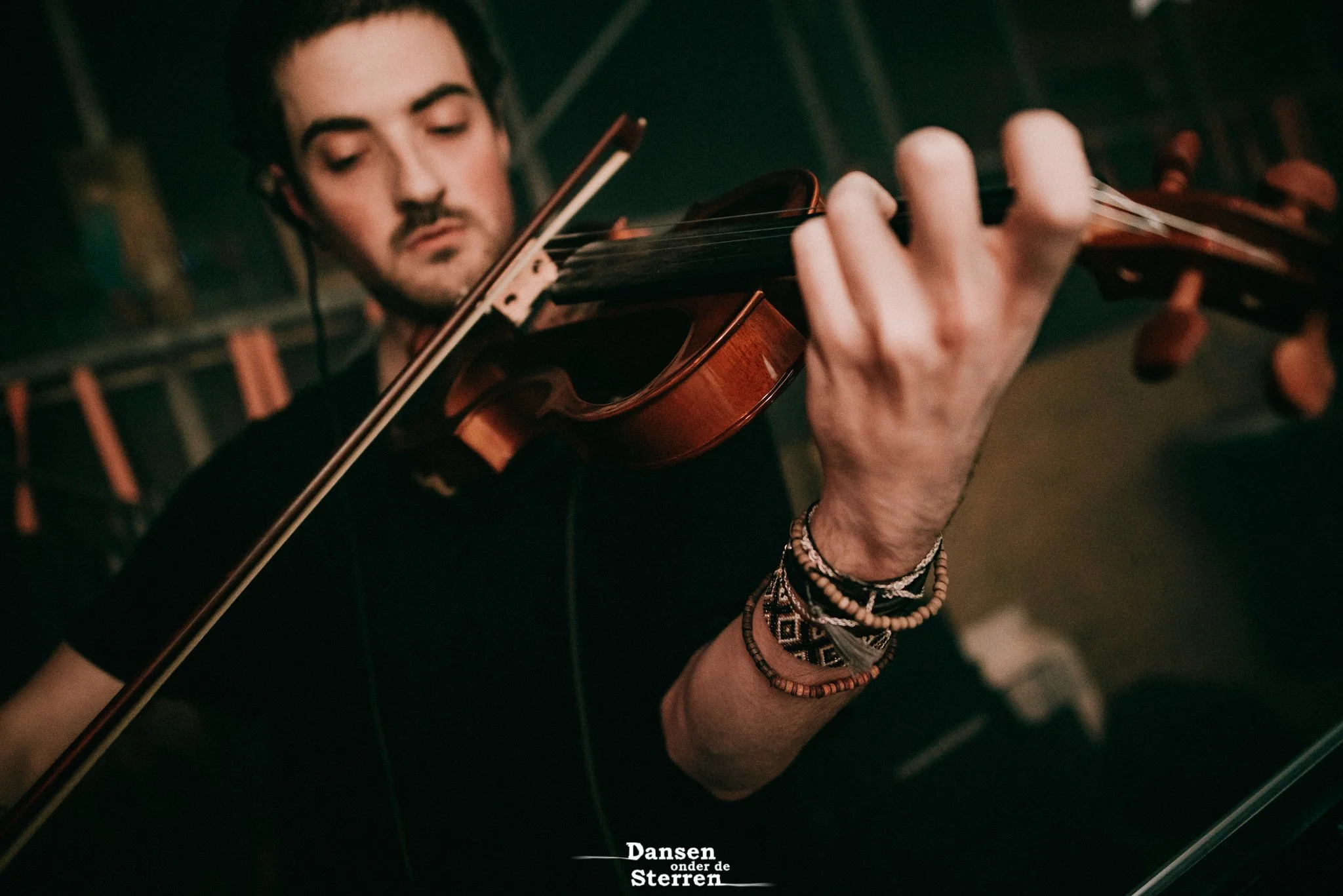 Close-up of a young man playing a violin, focusing on his face and hand, with a background indicating an indoor performance setting.