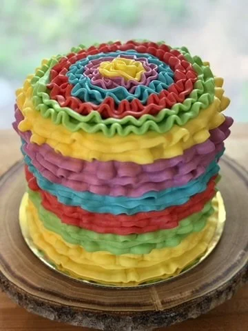 Stacked colorful ruffled cake with rainbow layers on a wooden table