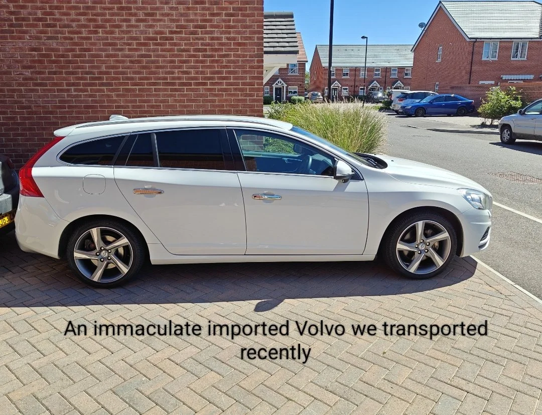 A white Volvo station wagon parked on a paved driveway beside a brick house in a residential neighborhood.