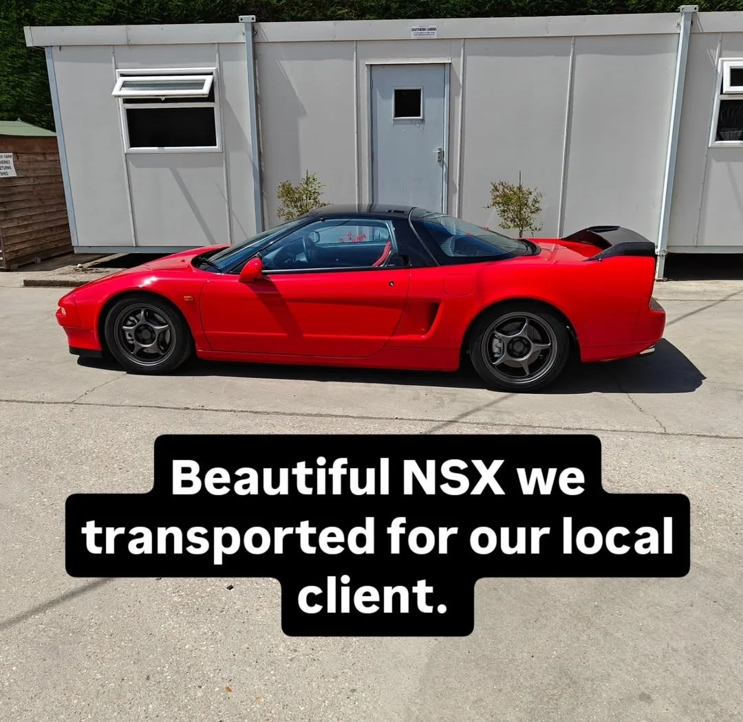 A red Nissan NSX sports car parked in front of a white portable building with two small plants and a gray door.