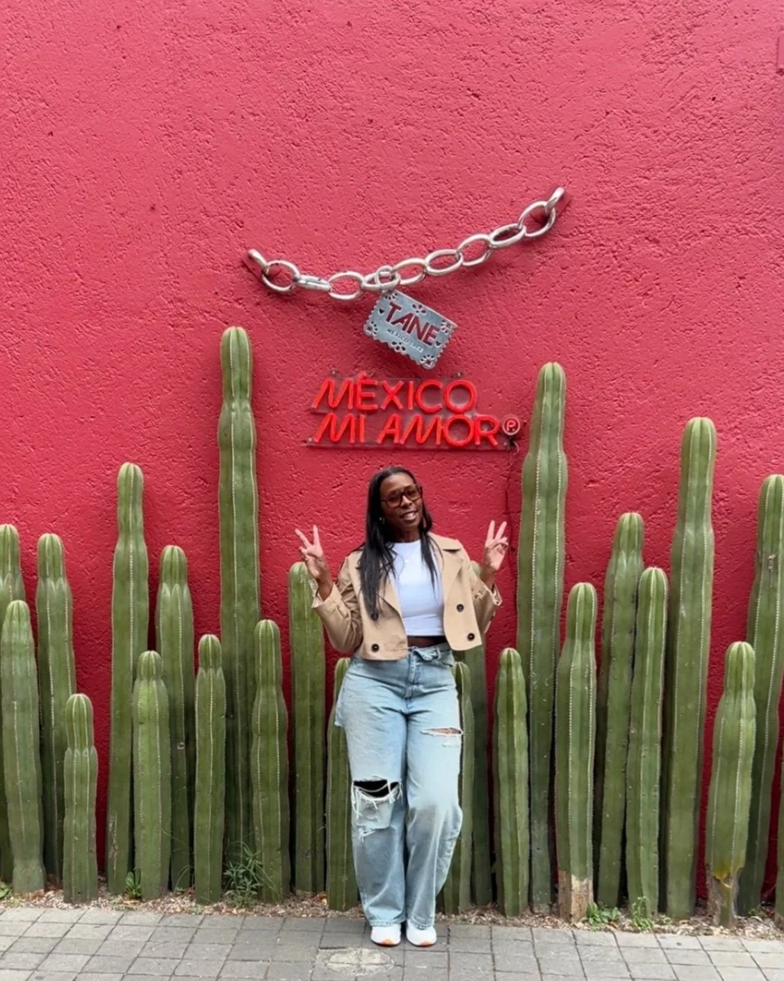 Black woman standing against a red wall in mexico holding up the peace sign