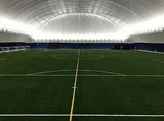 An indoor soccer field with artificial turf and a high, curved ceiling with bright lighting