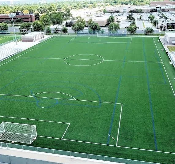 Aerial view of a new soccer field on a campus or sports complex, with goalposts, marking lines, and surrounding trees and buildings.