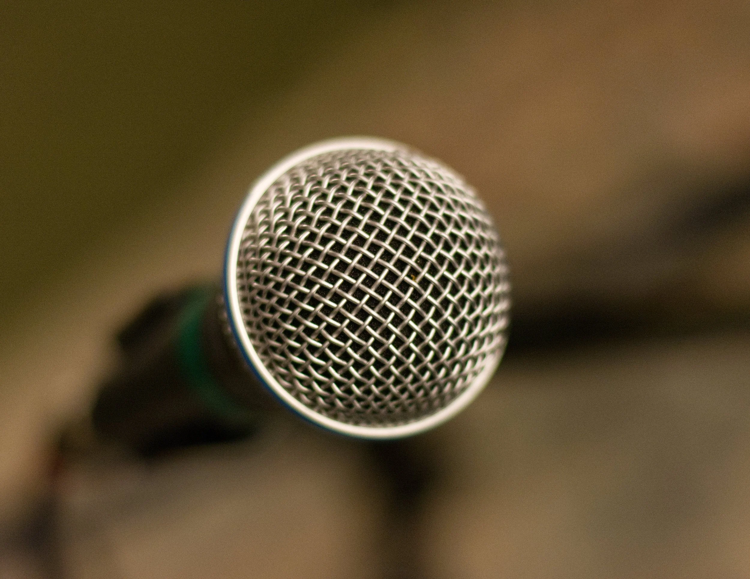 Close-up of a microphone with a metallic grille, positioned slightly to the left against a blurred background.