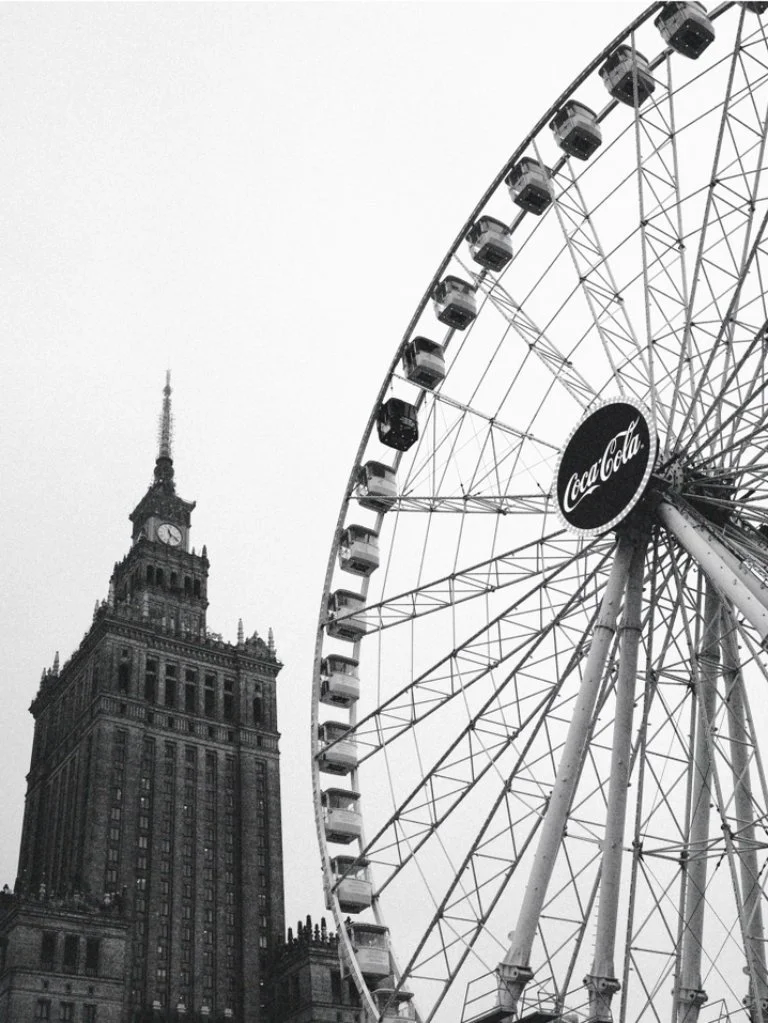 A black and white photo of a city scene with a tall historic building and a large Ferris wheel with a Coca-Cola sign.