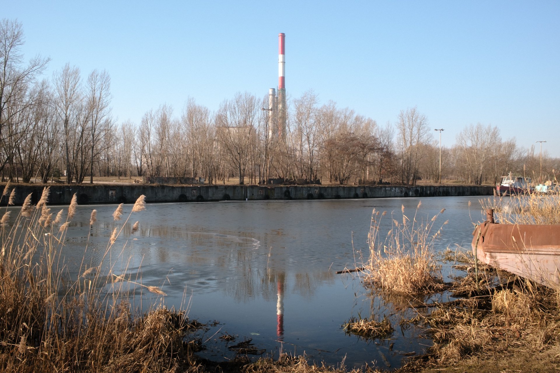 Biało-czerwony komin elektrociepłowni Żerań z odbiciem w wodzie Kanału Żerańskiego w Warszawie.