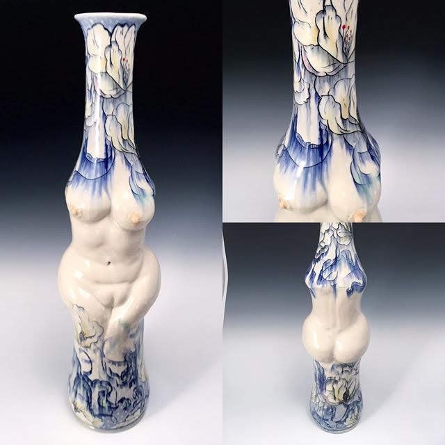 A ceramic vase with a design resembling a female torso, with the upper part decorated with floral patterns in blue and white.