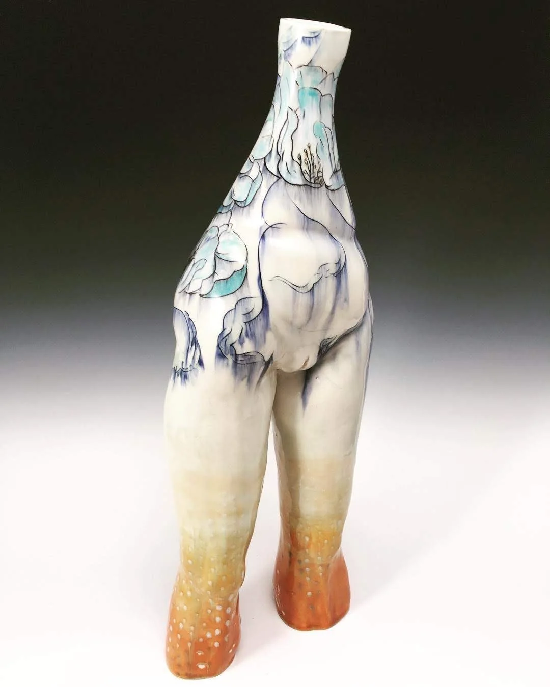 A ceramic sculpture of a standing female figure with a tilted head, featuring floral designs in blue and white on the upper body and orange and white on the lower legs.