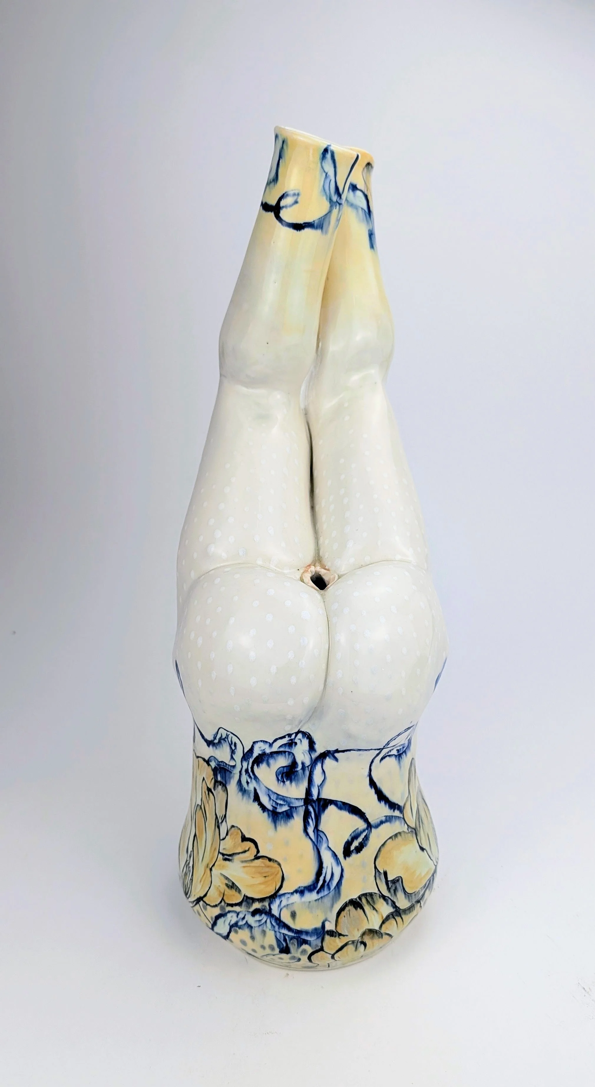 Ceramic vase with a design of a body of a woman with legs raised upward, featuring a polka dot pattern and floral motif in blue and yellow.