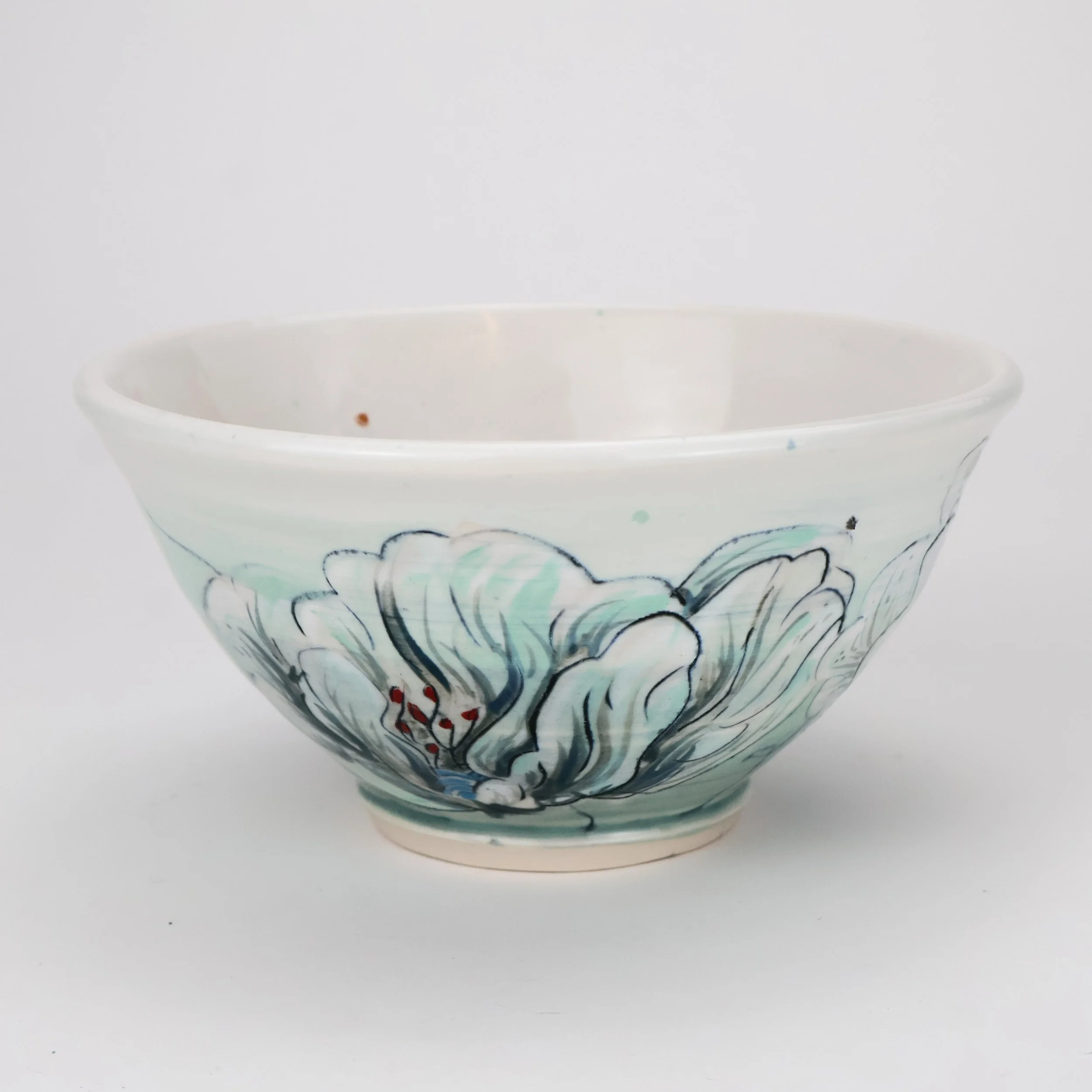 White ceramic bowl with hand-painted blue and black floral design and red accents, on a white background.