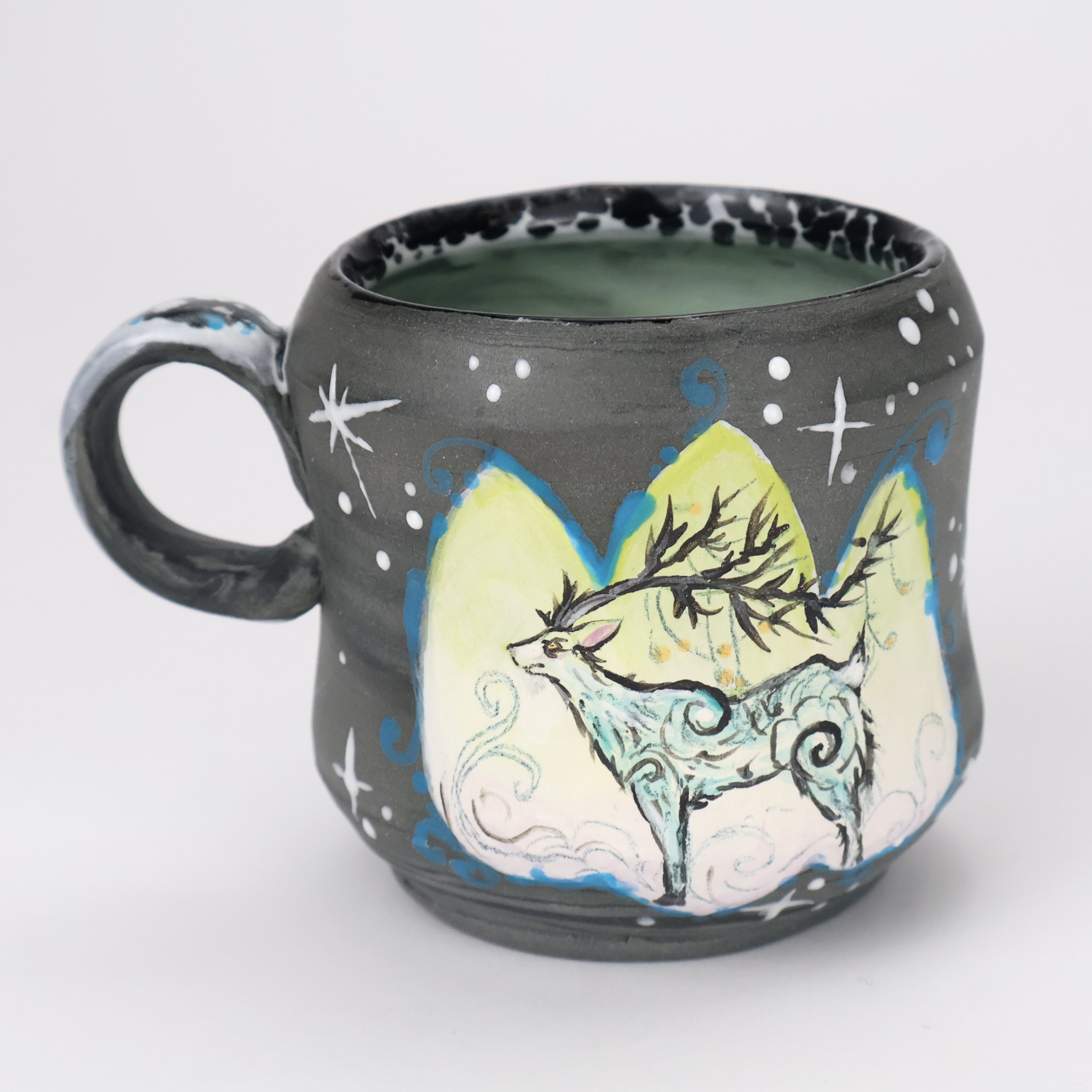 Decorative ceramic mug with a painted mythical creature resembling a deer with swirling patterns, set against mountains and starry night sky.