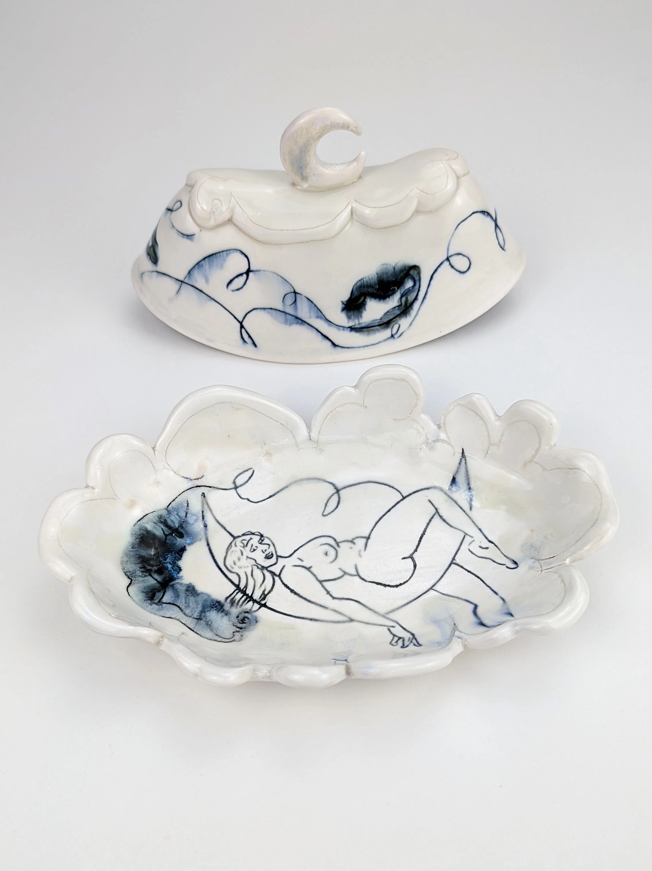 Decorative ceramic butter dish and matching lid with hand-drawn illustrations of a female figure on a cloud, featuring a moon handle and clouds in a blue and white glaze.