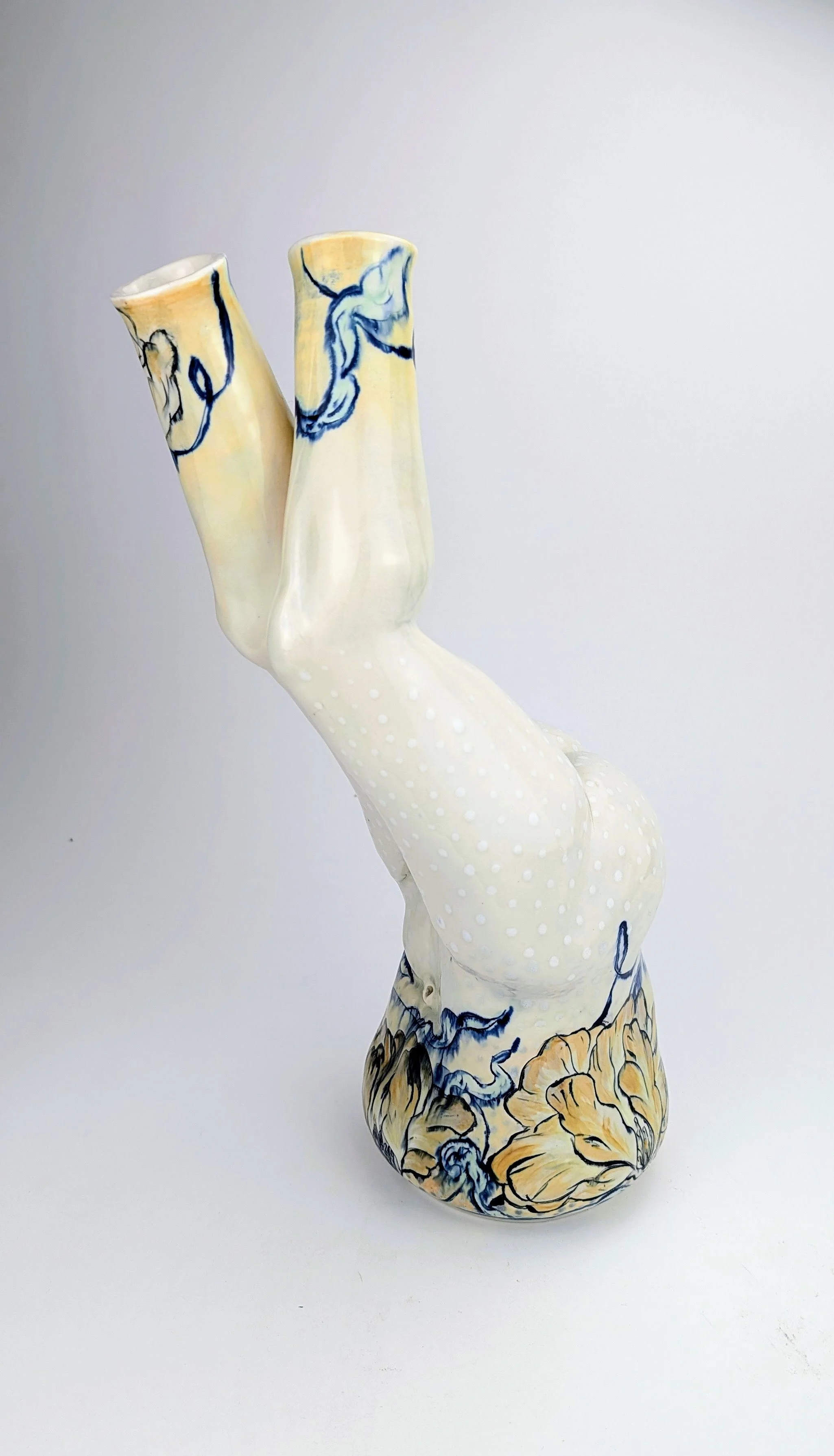 A ceramic sculpture of a female figure with legs raised upside down, decorated with blue, beige, and white patterns.