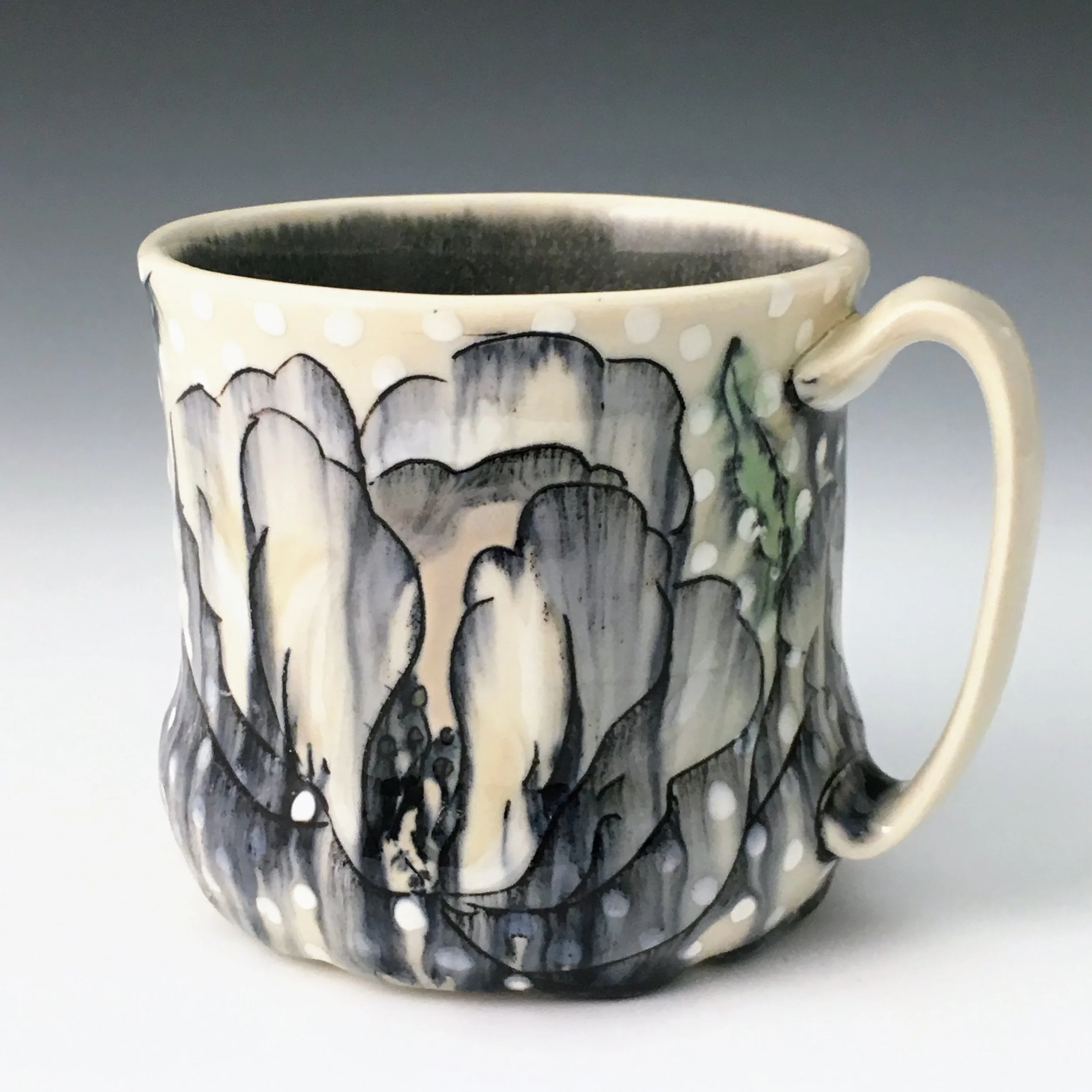 Hand-painted ceramic mug with floral design in black, white, and beige, with white polka dots on the upper border and a curved handle.