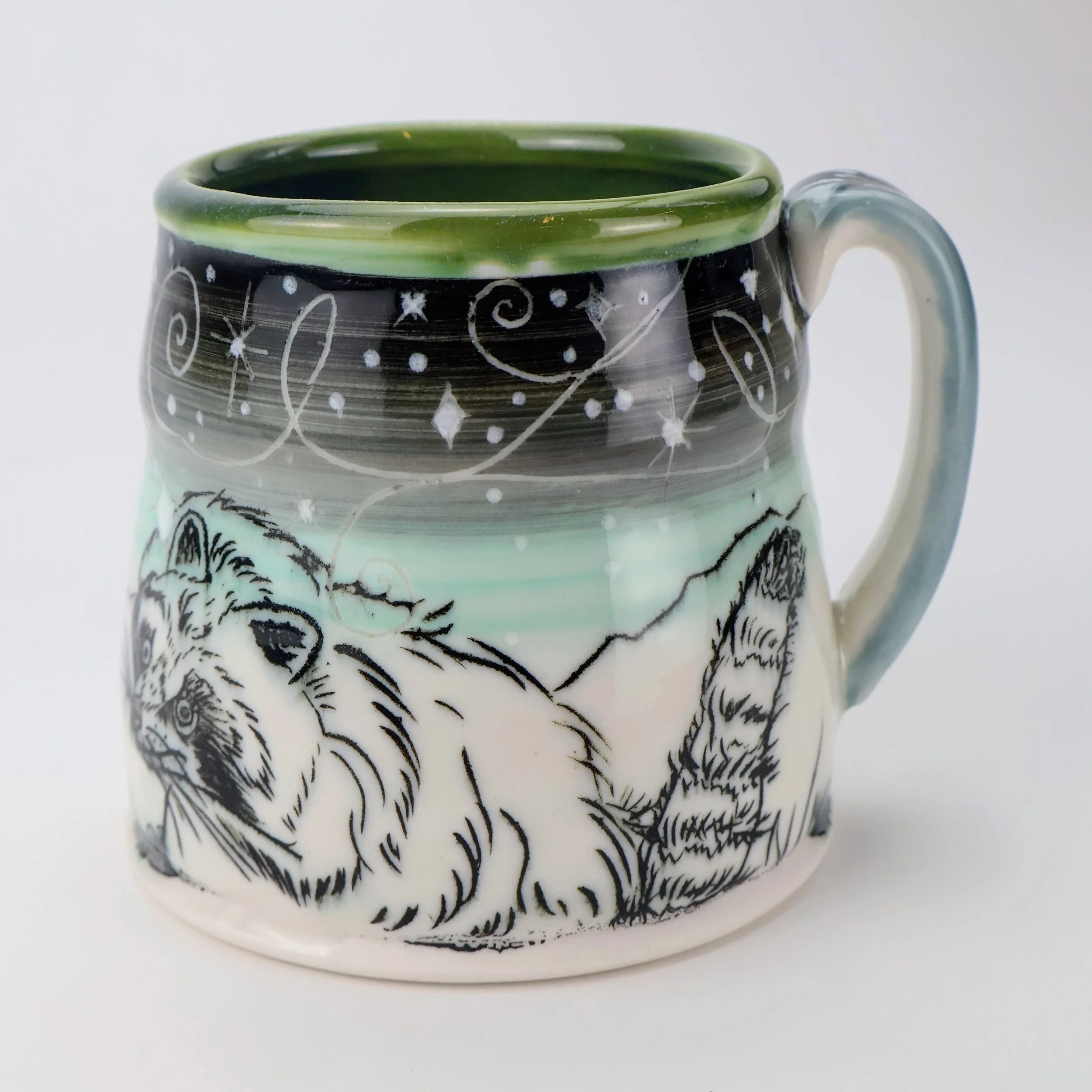 Ceramic mug with a snowy mountain landscape, black and white racoon illustration, and celestial patterns of stars and swirls in black and white.