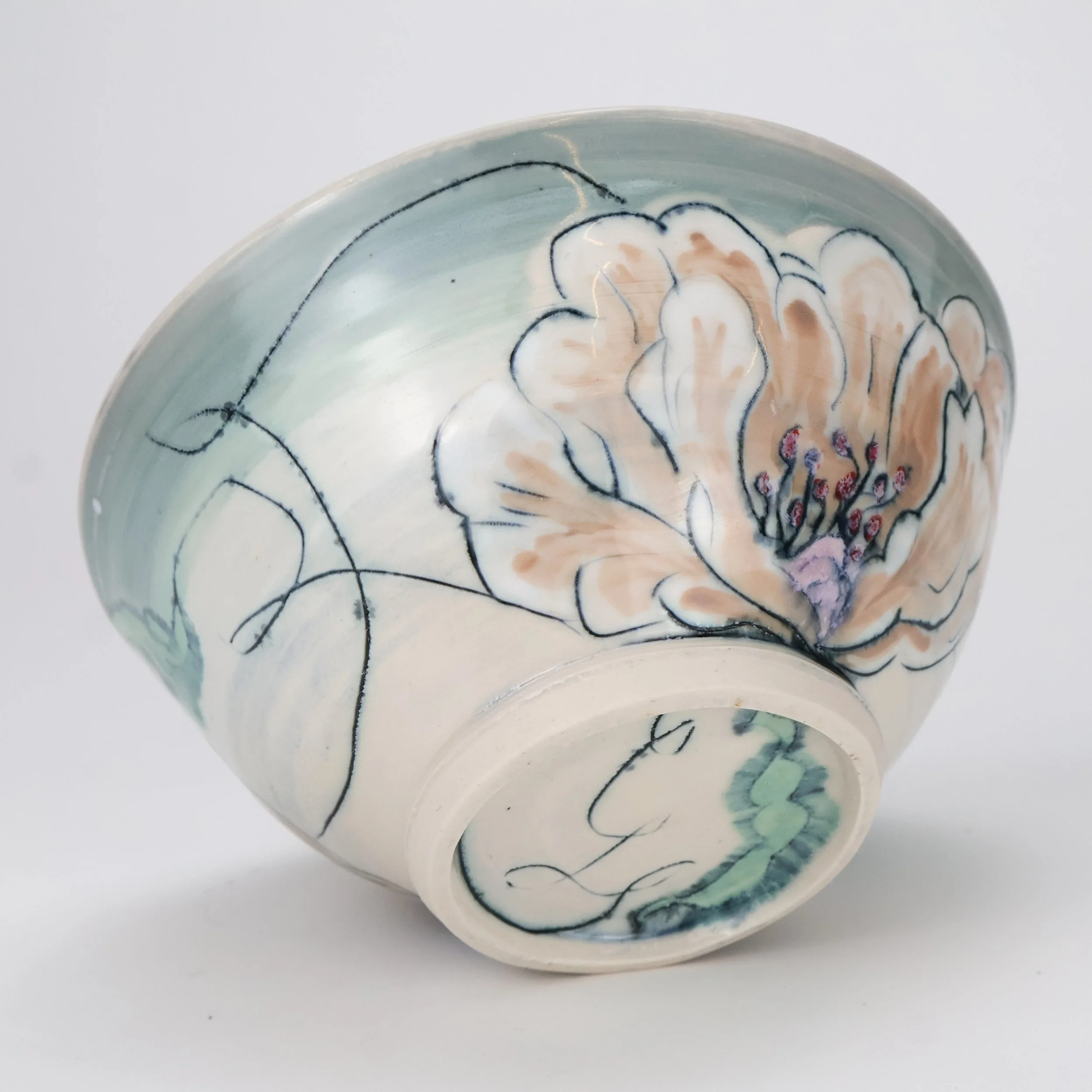A ceramic bowl with hand-painted floral design featuring a large Mishima inlaid peoneis with black outline and purple stamen, green leaves, and black lines on a light cream background.