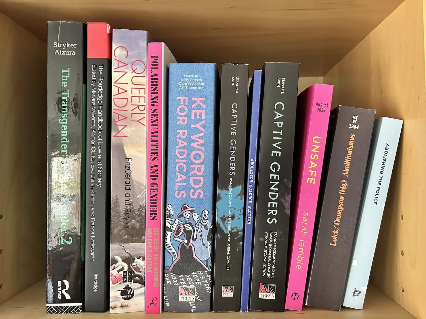 A bookshelf containing research and academic books, including titles on transgender rights, law, sociology, and police abolition.