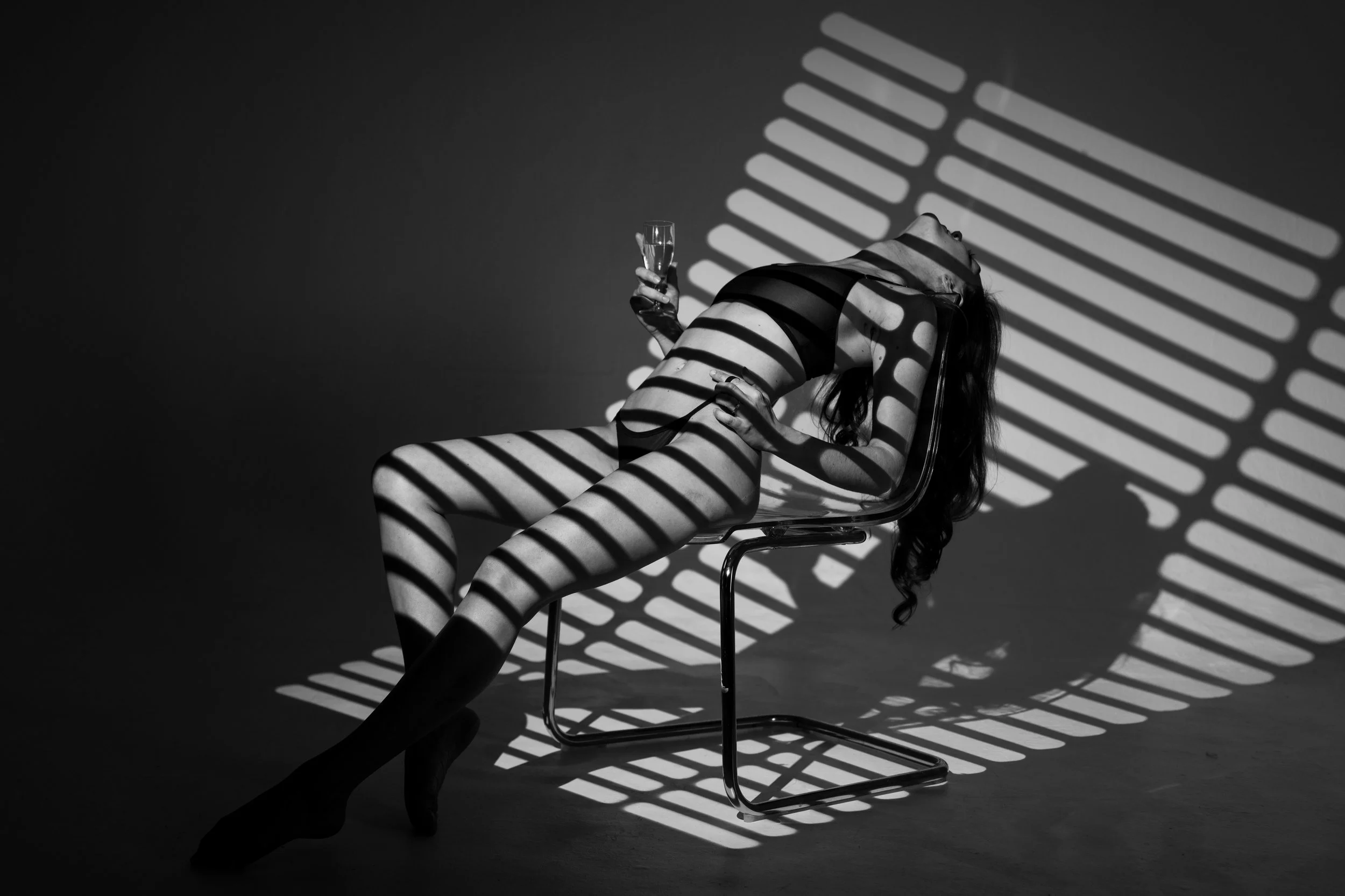 Schwarzweiß Bild einer Frau im Schatten einer Jalousie. Die Frau hält ein Sektglas in der Hand.
