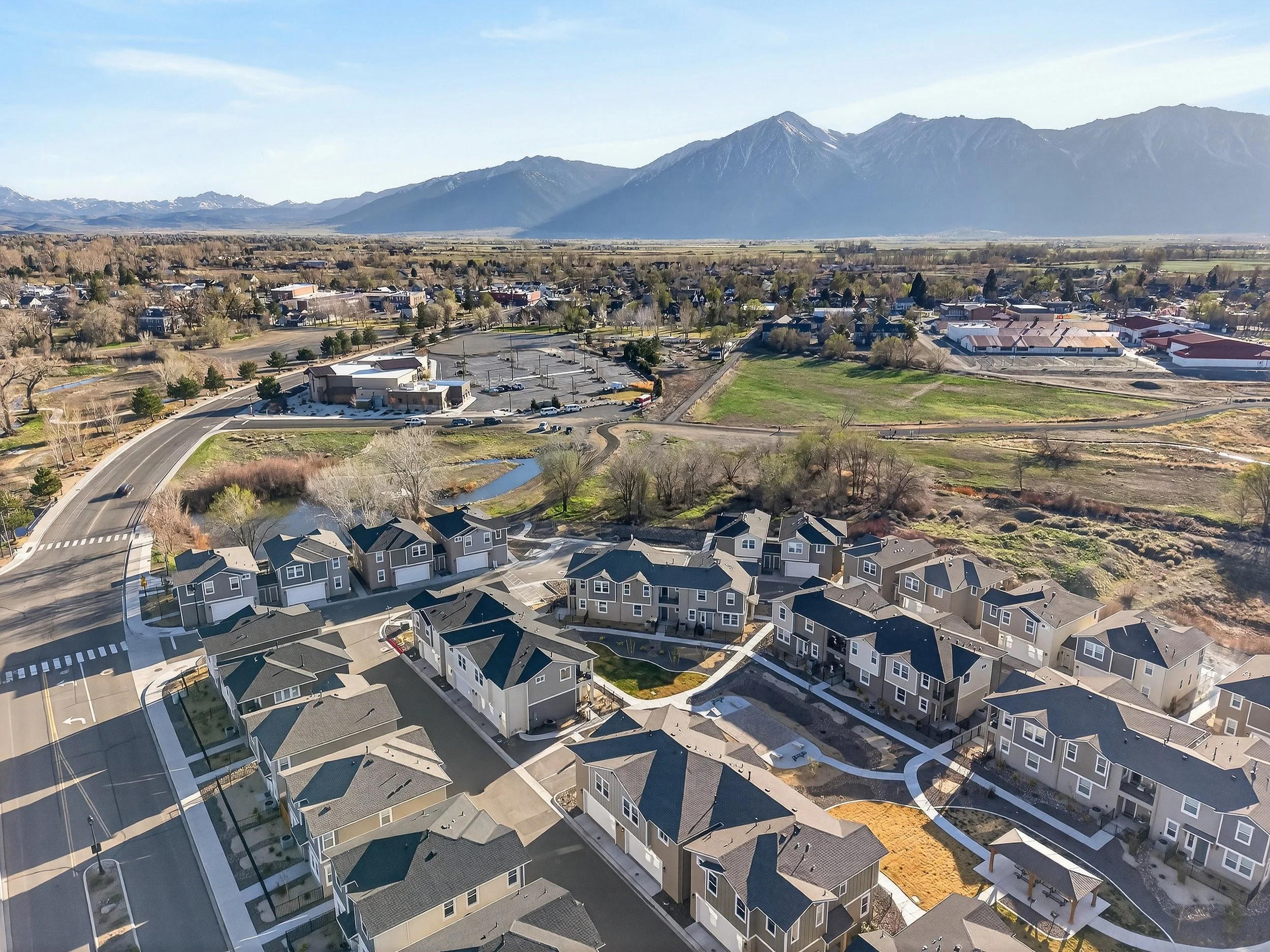 Aerial view of a suburban neighborhood with houses, roads, trees, and a field, with mountains in the background and a clear blue sky.  Carson Valley, Minden, Gardnerville, Nevada.