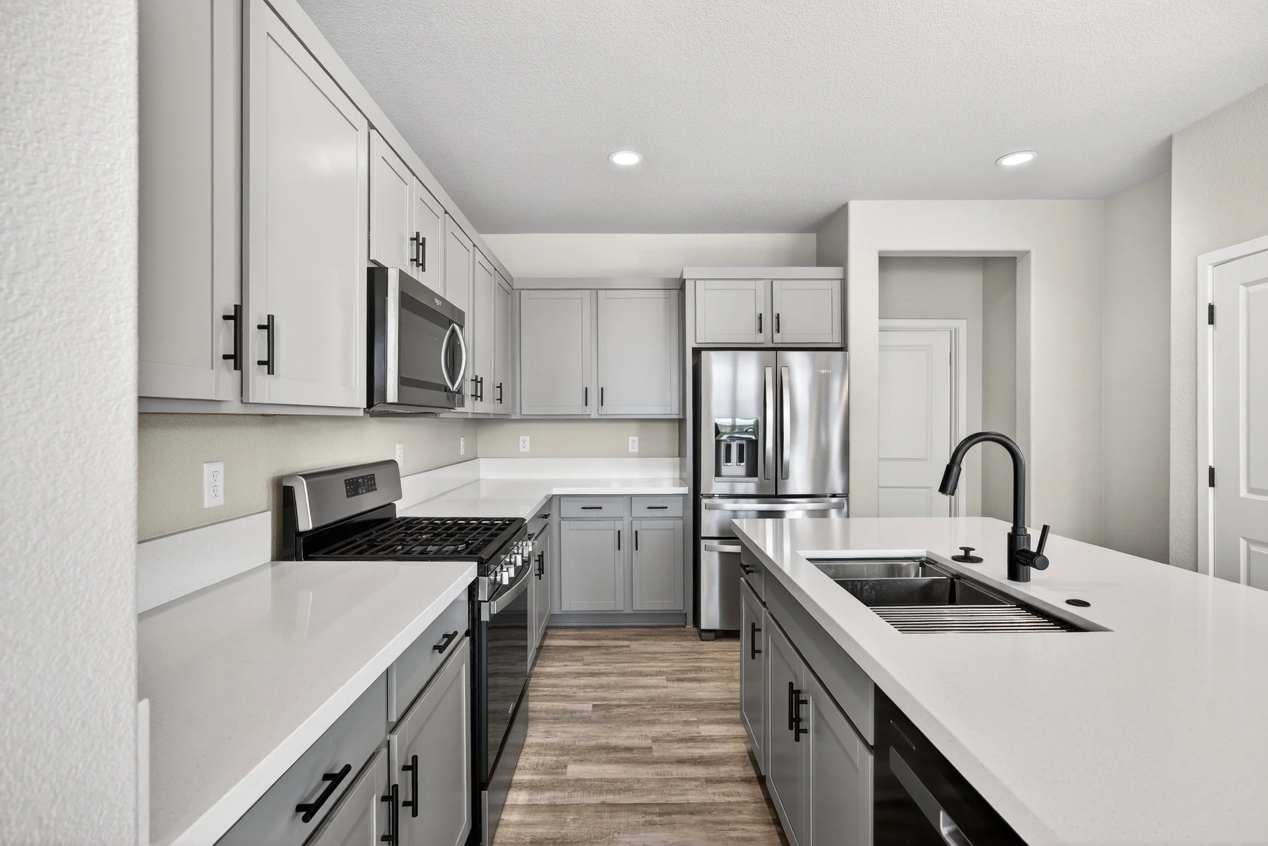 Modern kitchen with gray cabinets, stainless steel appliances, white countertops, and wood flooring.