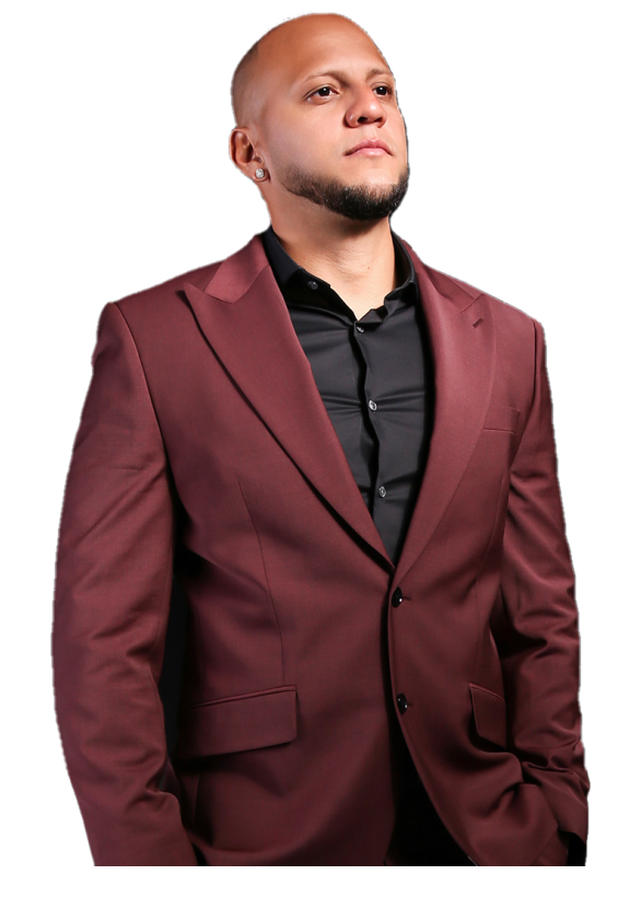 A man with a shaved head and goatee, wearing a burgundy suit jacket over a black shirt, looking confidently to the side against a dark background.
