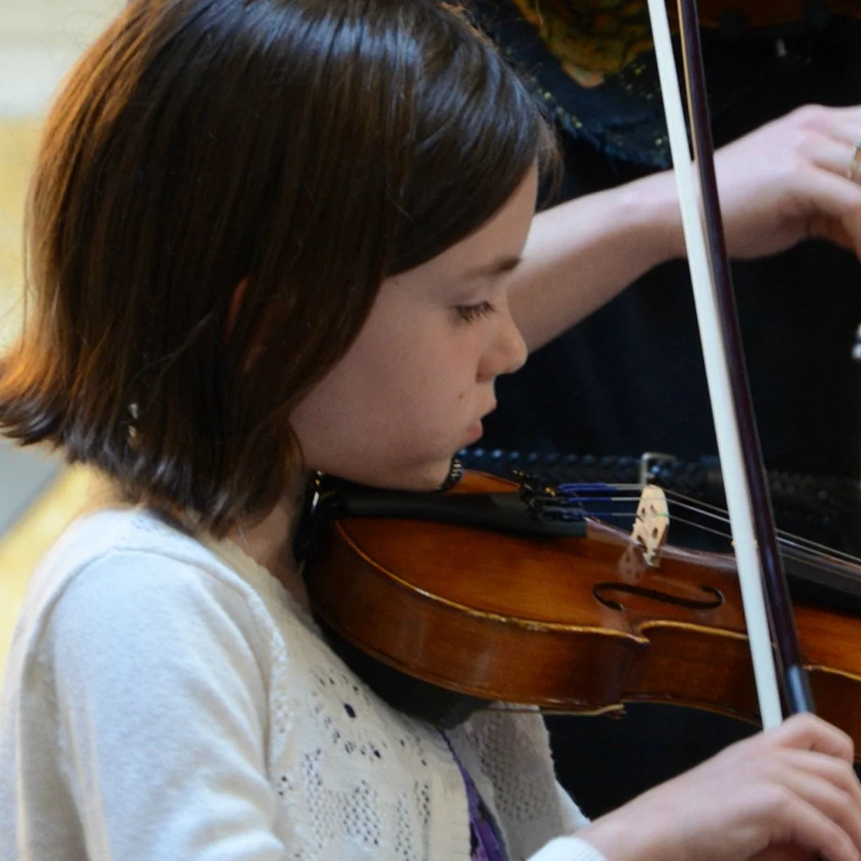 A young girl with shoulder-length brown hair playing the violin, with her focus on the instrument.
