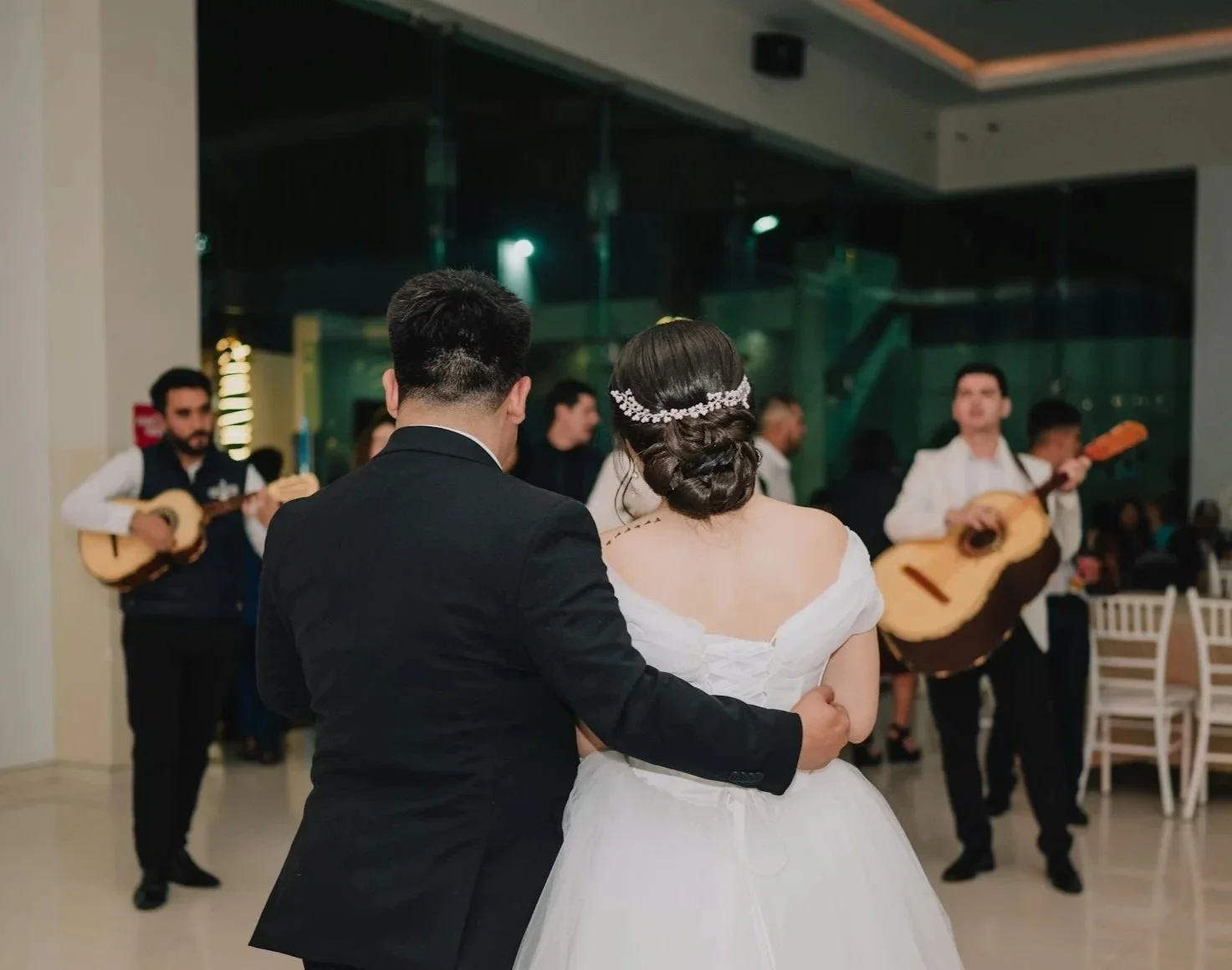 A bride and groom dancing at their wedding reception, with musicians playing guitars in the background.