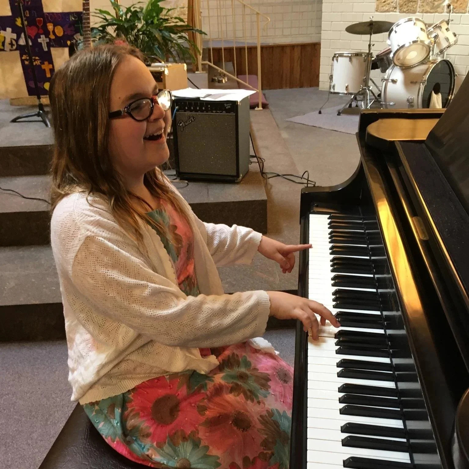 A smiling young girl with glasses playing a grand piano in a music room.