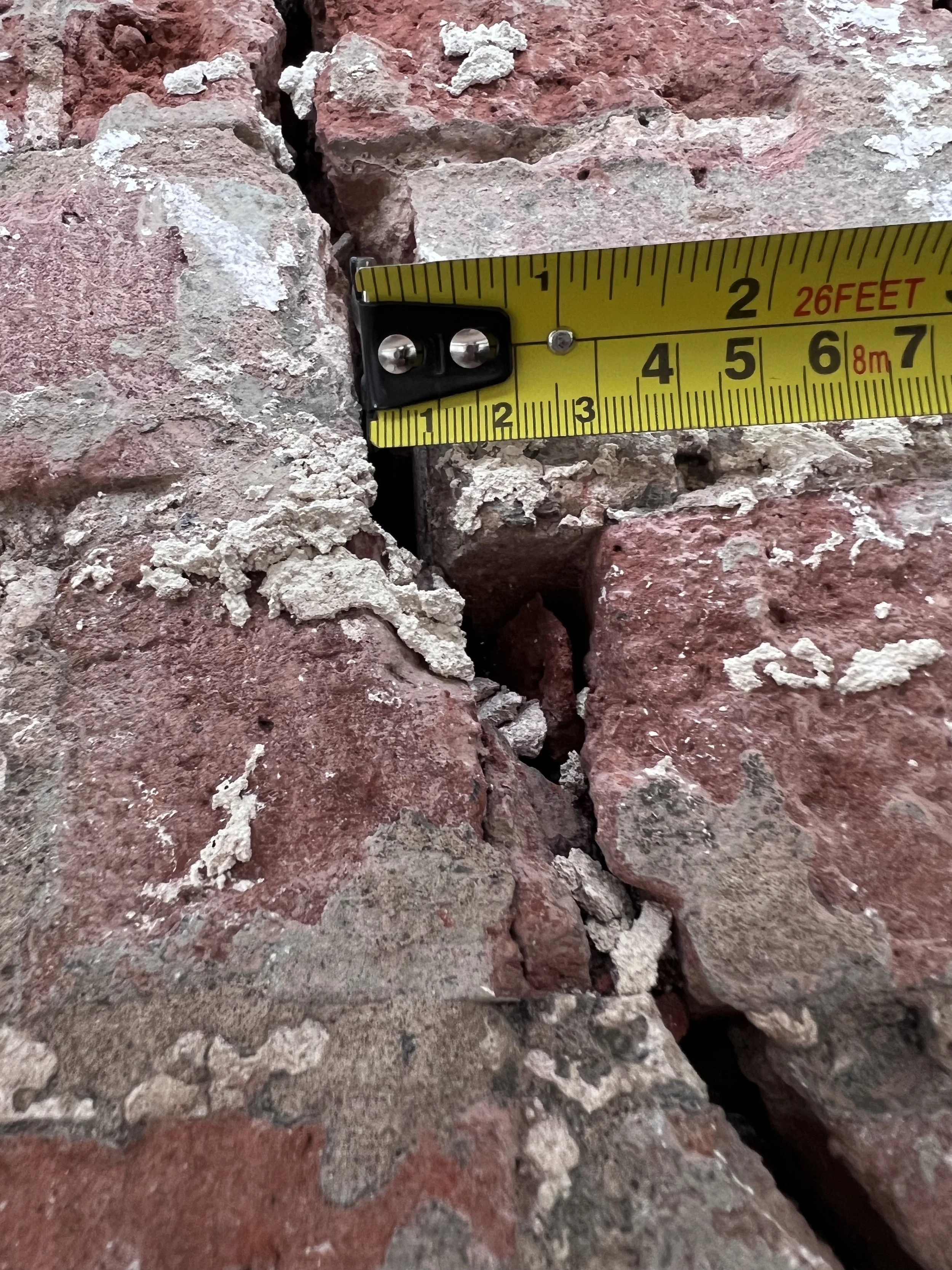 Close-up view of red and gray rocks with a yellow measuring tape extended over them, showing measurements in inches and feet.