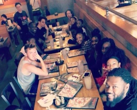 A group of diverse people sitting around a long table in a restaurant, enjoying food and drinks.
