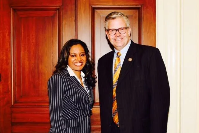 A woman and a man in business attire standing next to each other indoors, smiling at the camera.