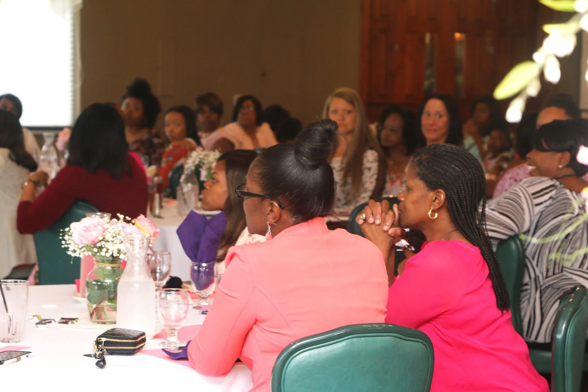 Women sitting at a banquet table, listening attentively to a speaker at a formal event or conference.