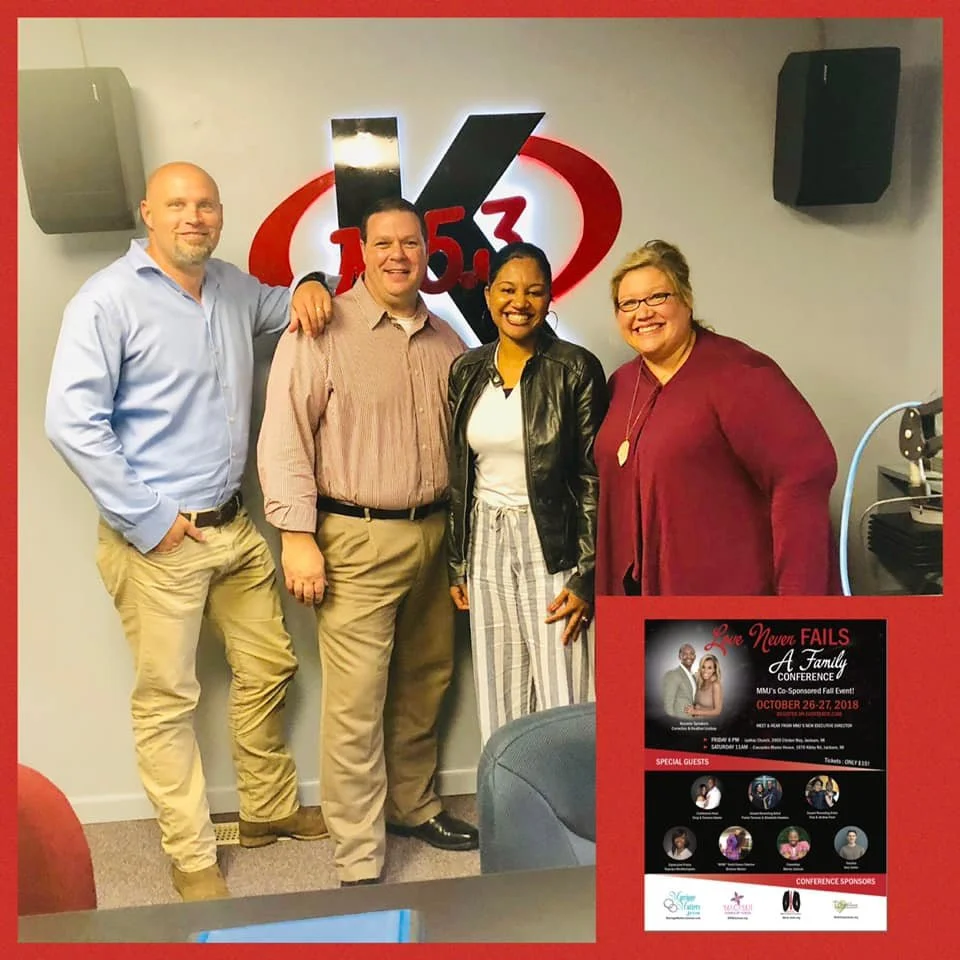 Four people standing together in a radio station studio, smiling at the camera. A large logo with '105.3' is displayed behind them on the wall, flanked by two speakers. A promotional poster for a family conference is on the bottom right of the image.