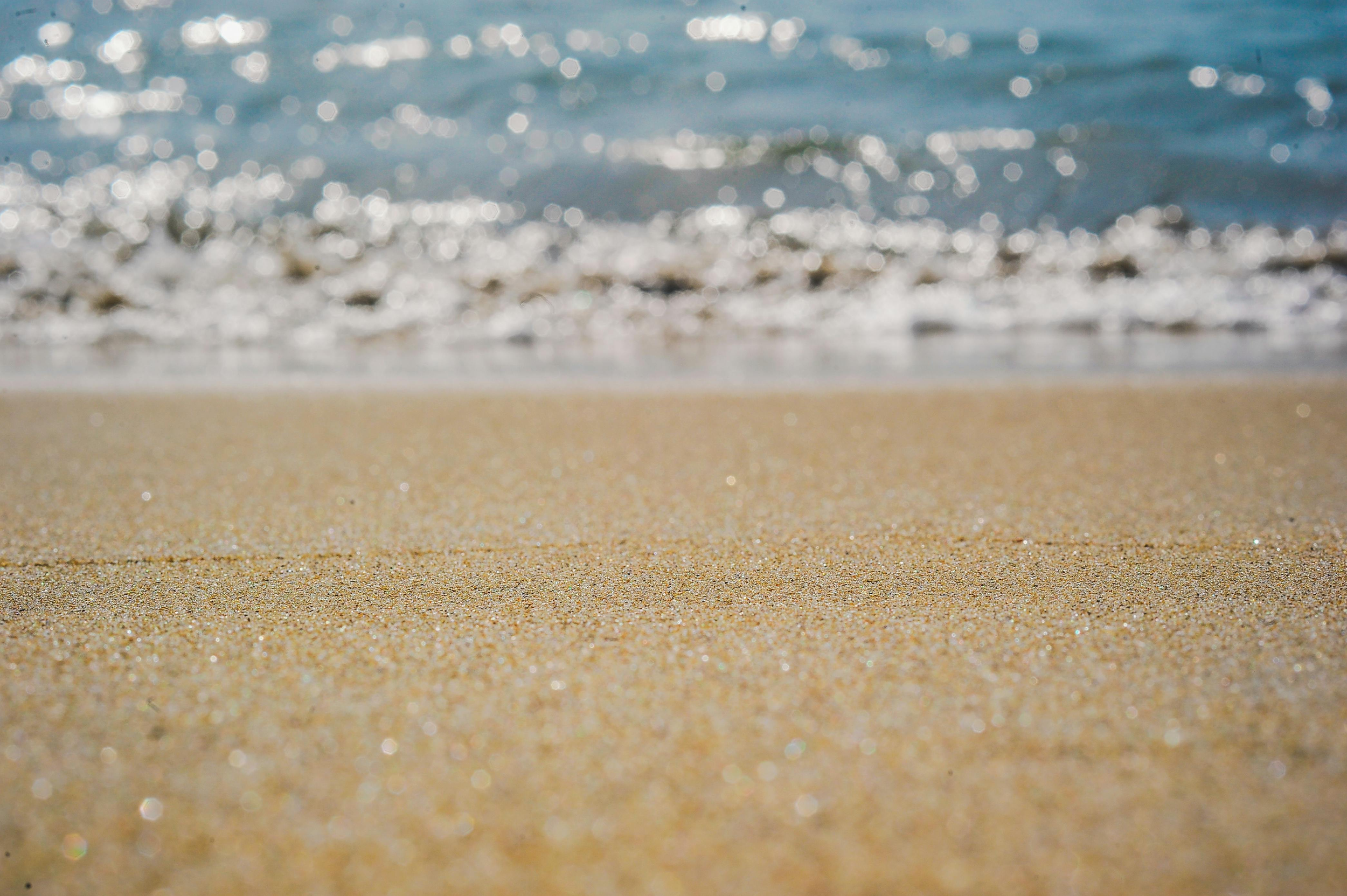Close-up of a sandy beach with small waves and sparkling water.