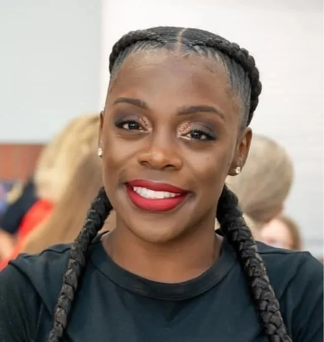 Smiling woman with braided hair and red lipstick in a casual setting.