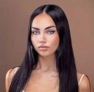 A woman with long black hair and blue eyes, wearing a sleeveless top, against a neutral background.