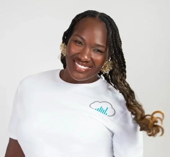 A smiling woman with long braids wearing a white t-shirt with a cloud logo and wireless earbuds, posing against a plain white background.