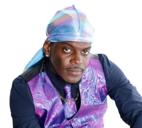 A man wearing a colorful bandana, a golf shirt, and a purple vest with paisley patterns.